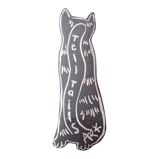 The back of a black cat shaped bookmark with the text 'tell tails' written down the centre in silver writing.