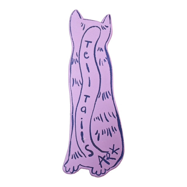 The back of a lilac cat shaped bookmark with the text 'tell tails' written down the centre in purple writing.