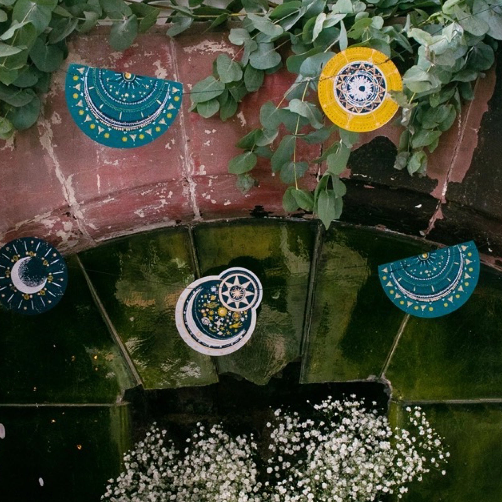 Celestial space garland with paper moons and star constellations in various green, gold and silver designs hanging in a fireplace.