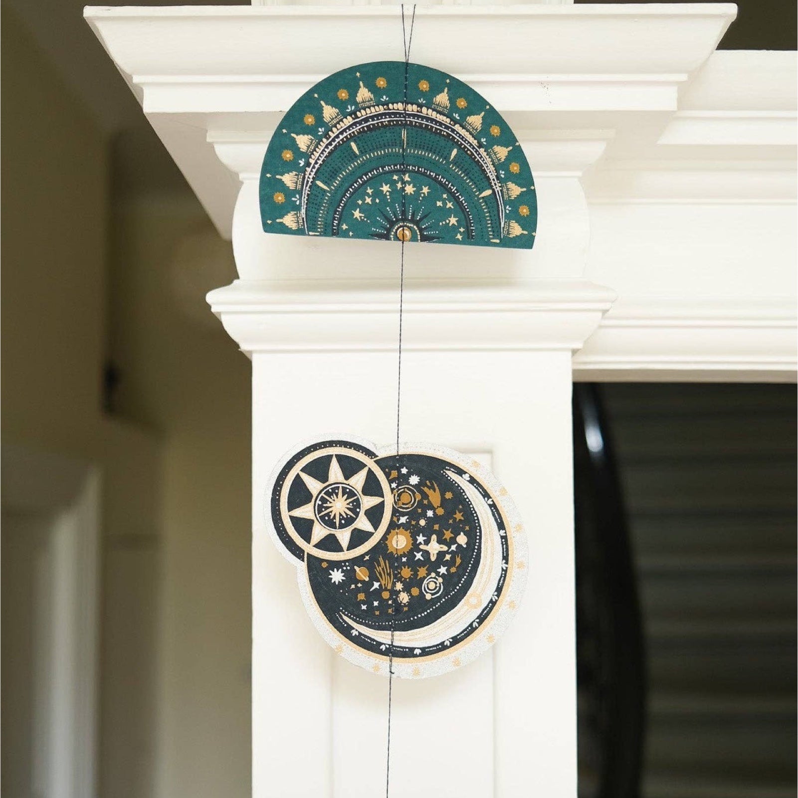 A celestial paper garland with nine screen-printed paper stars and moons in teal, navy, gold and silver designs hanging down a banister.