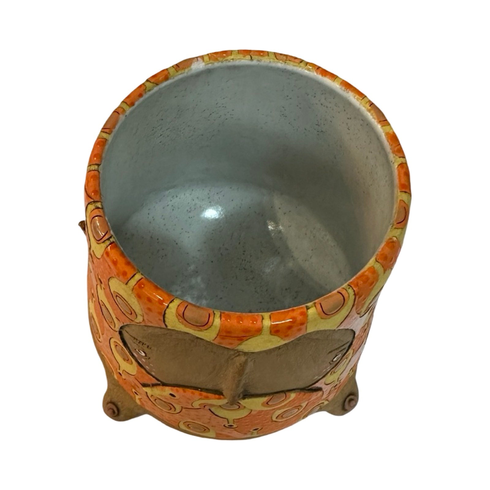 The top of a ceramic beaker with a male moustached face and a mustard and brown paddles pattern on an orange background.