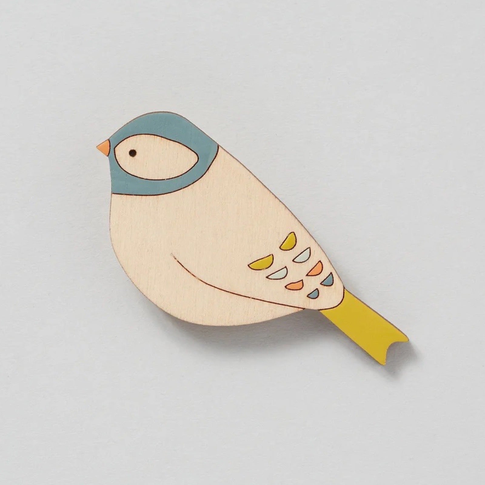 Wooden bird-shaped brooch with colourful design on a light grey background.