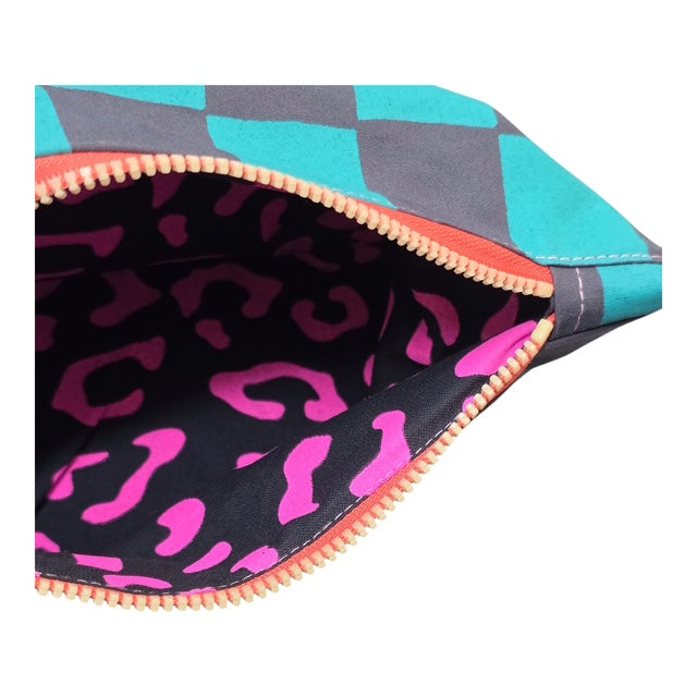 A screen-printed checked cosmetic bag in turquoise and grey with a yellow zip open to show pink leopard print lining.