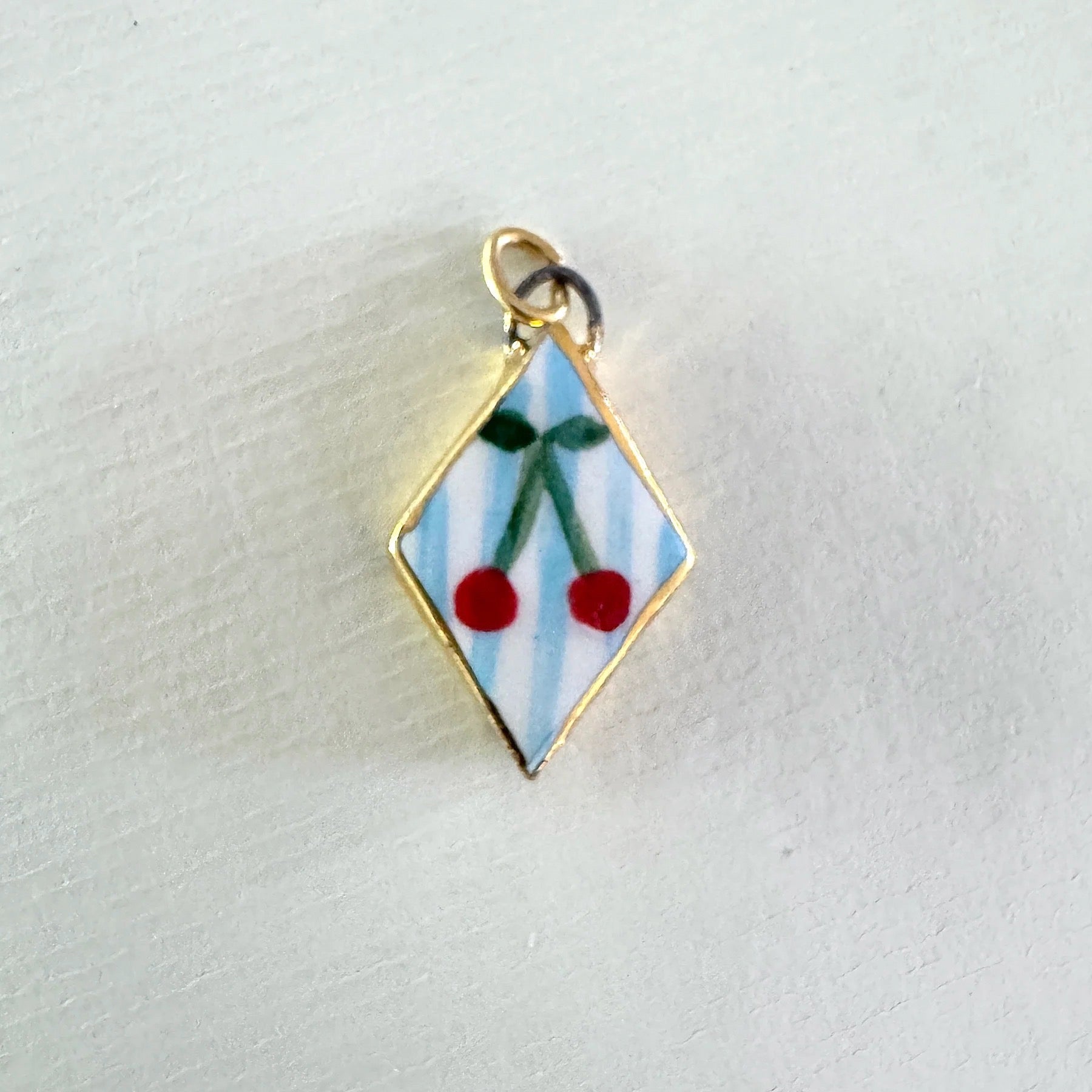 Diamond-shaped enamel charm with cherries on a light grey background.