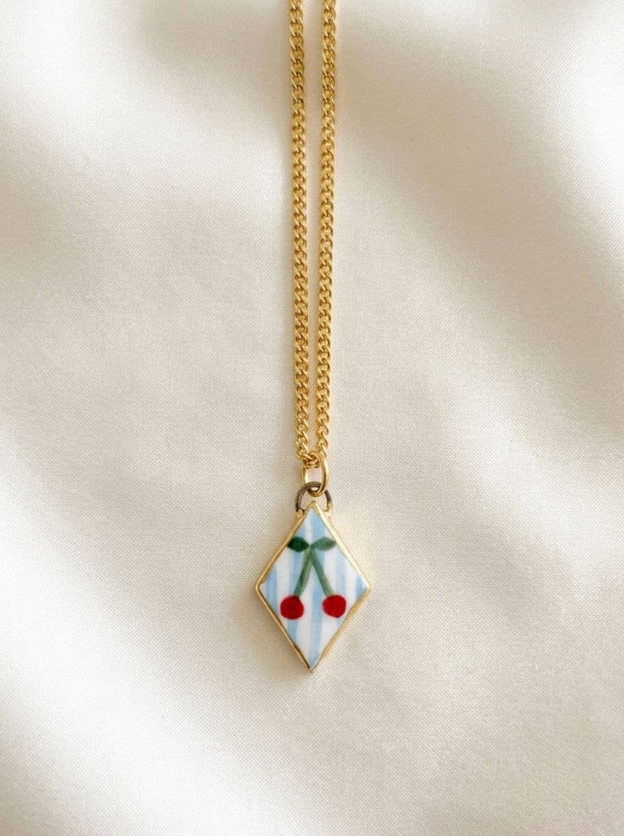 Necklace with a diamond-shaped pendant featuring cherries on a beige background.