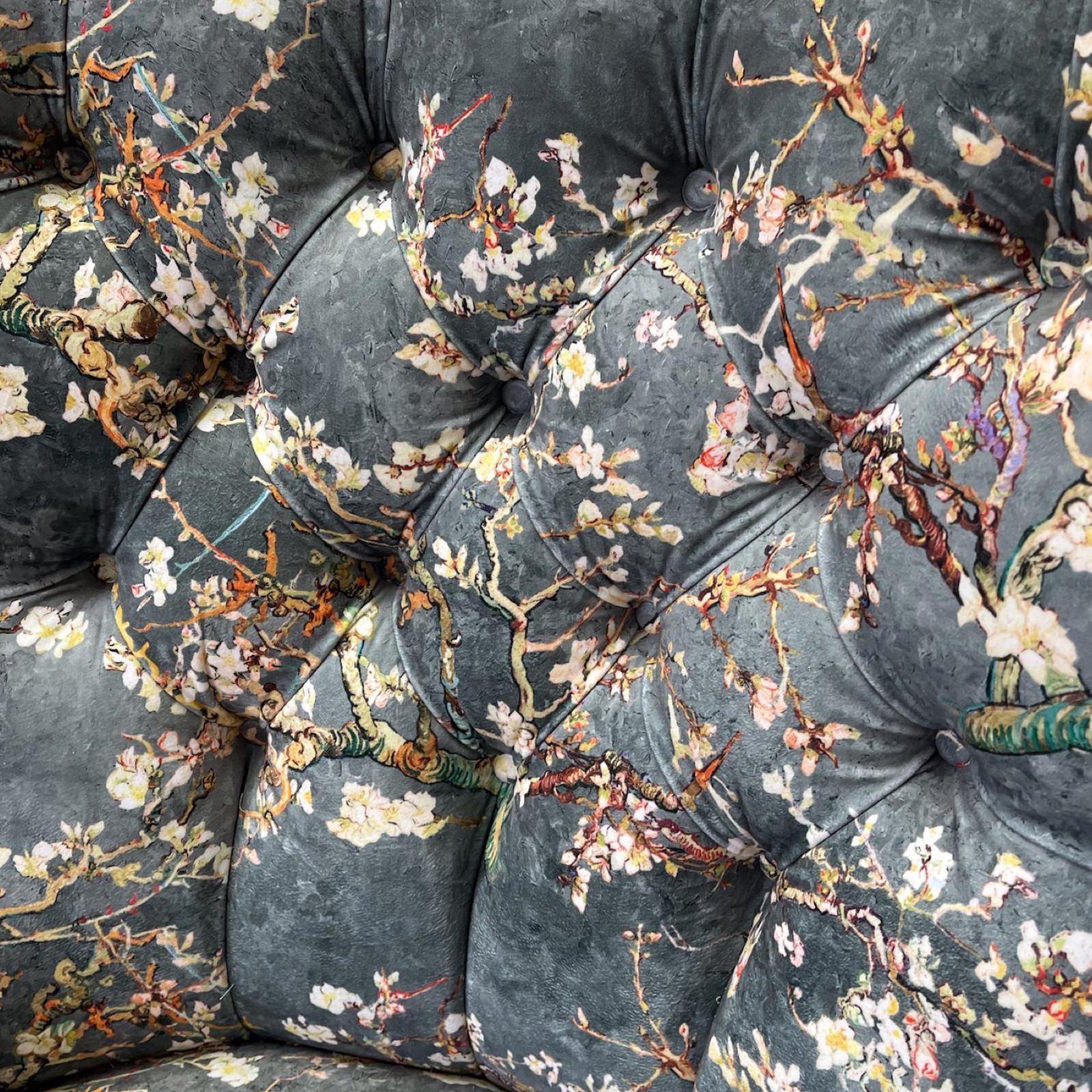A grey velvet armchair with a floral pattern of white cherry blossoms, featuring button-back tufting, grey binding, and mahogany legs with gold castors.