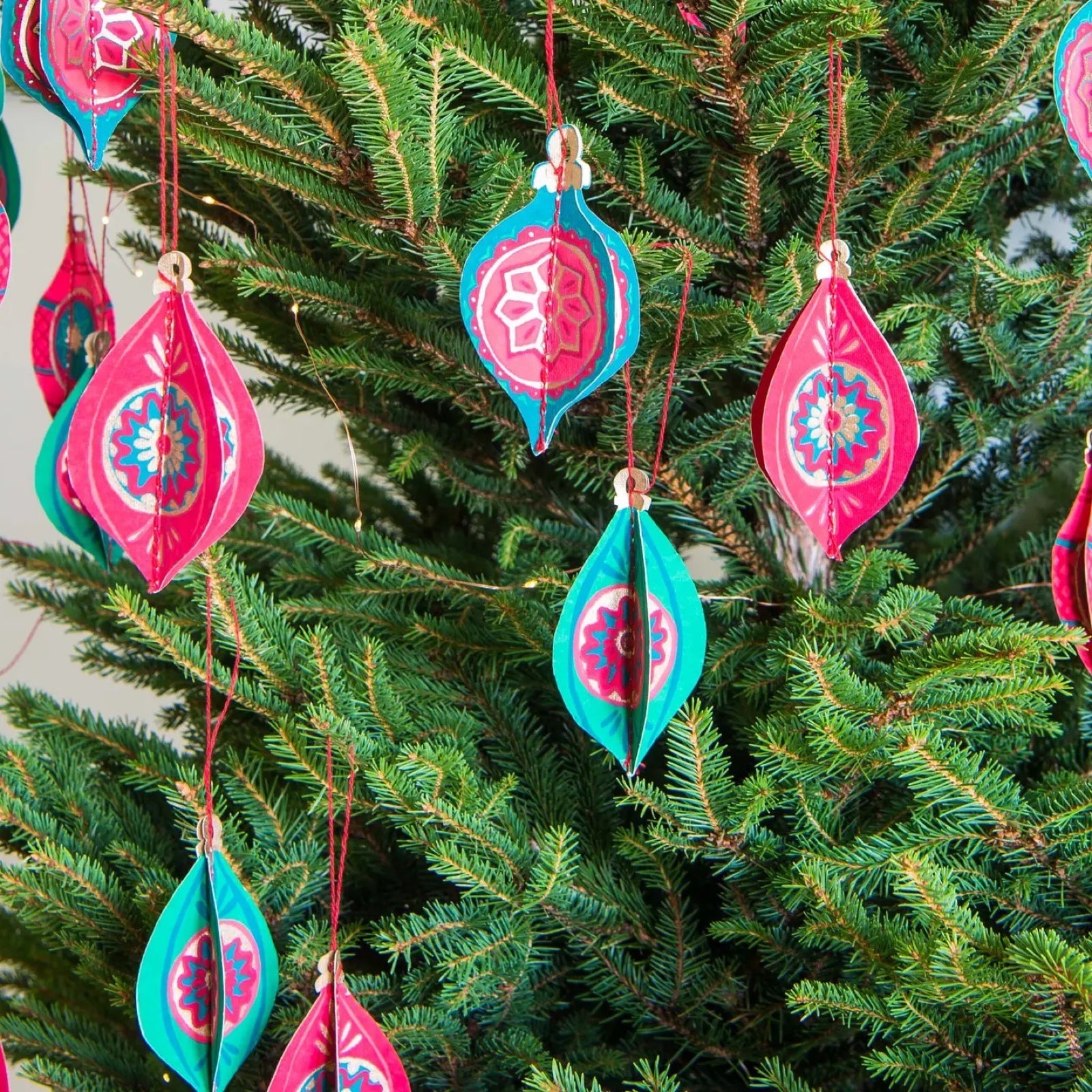 4 recycled paper bauble decorations in red, pink and green hanging on a Christmas tree.