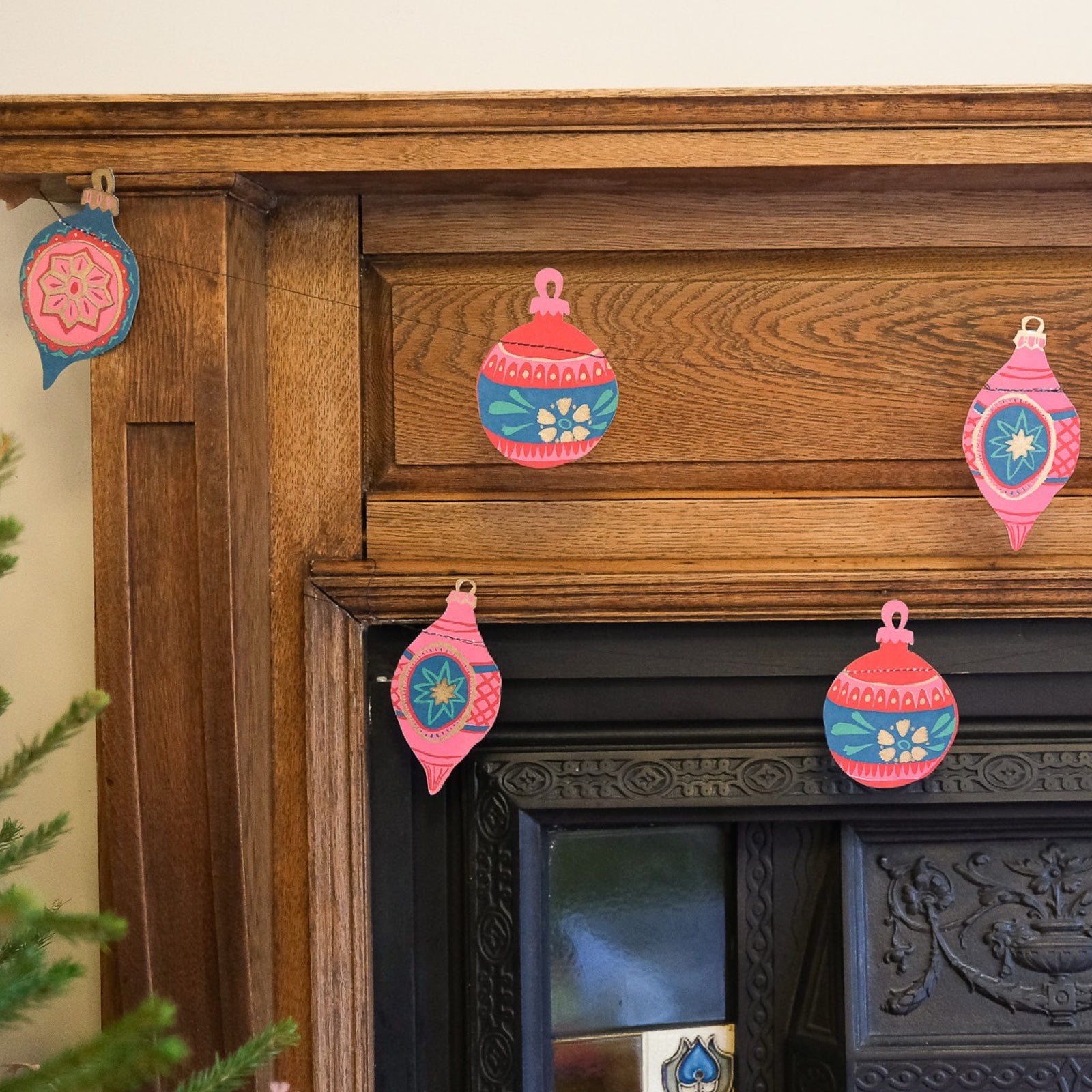 Christmas bauble garland with paper baubles in various red, green and gold designs hanging along a wooden fireplace.