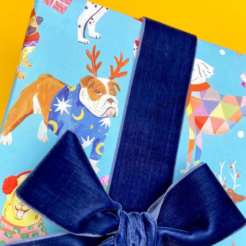Gift box with blue ribbon and colourful dog-themed wrapping paper on a yellow background.