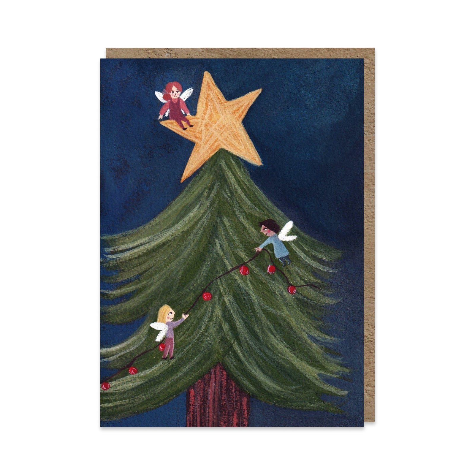 A vertical Christmas greeting card featuring three fairies decorating a green Christmas tree with red lights under a large gold star, shown against a dark navy background with a kraft envelope behind it.