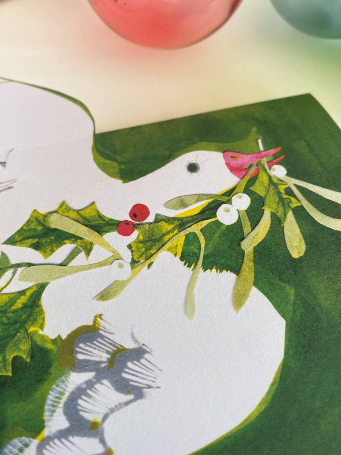 Card with a white goose holding mistletoe against a green background.