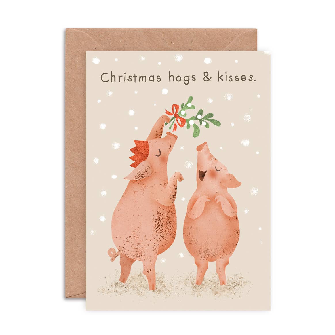 A Christmas greeting card with a kraft envelope behind it. The card has the text 'Christmas hogs & kisses' with a pig holding up mistletoe above another pig.