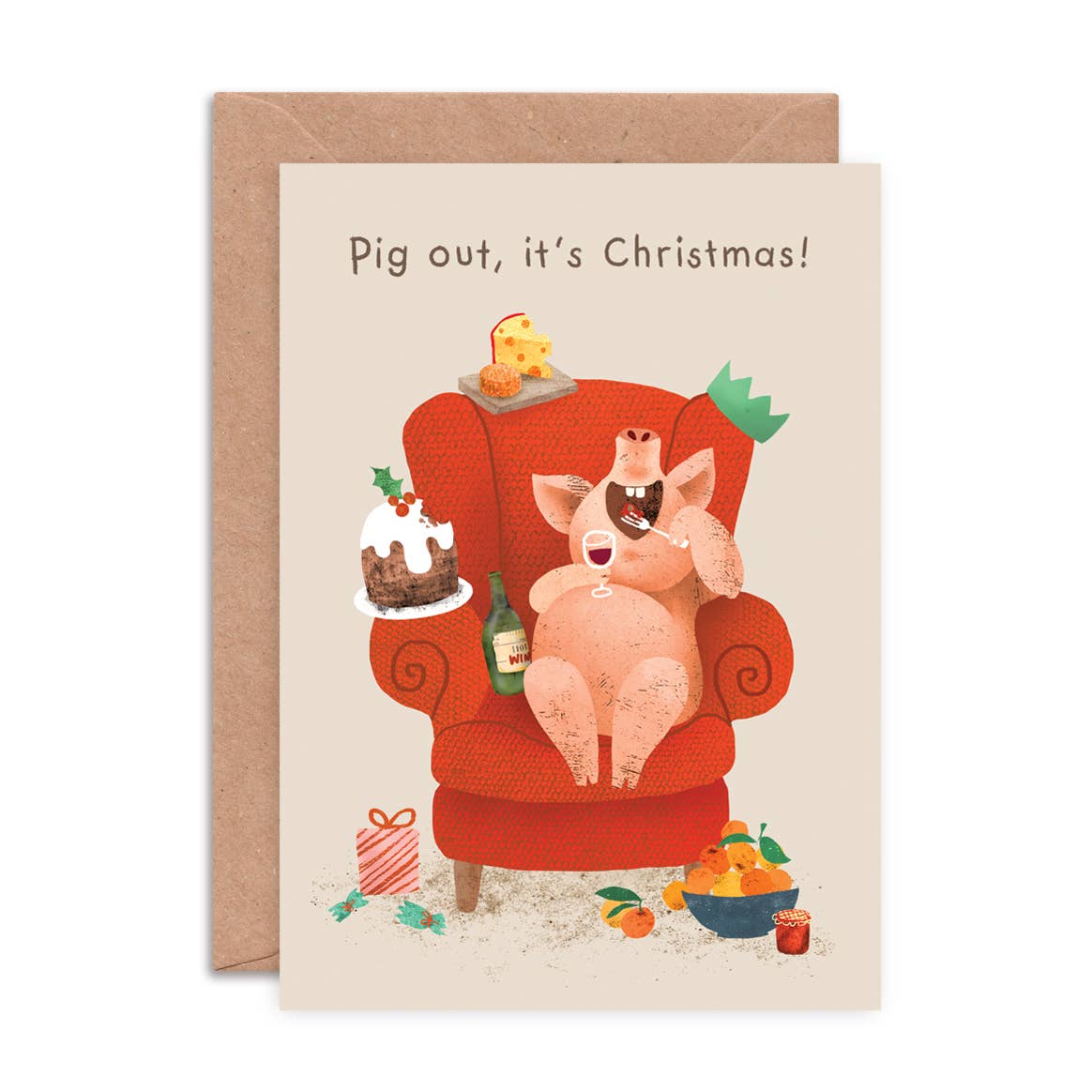 A Christmas greeting card with a kraft envelope, featuring a cartoon pig sitting in a red armchair surrounded by festive items, with the text 'Pig out, it's Christmas!' at the top.