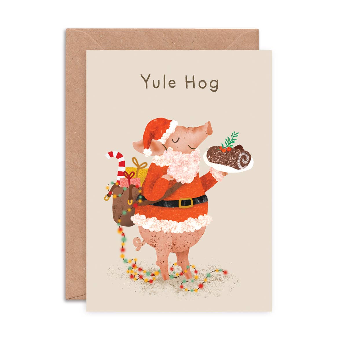 A Christmas greeting card featuring a cartoon pig dressed as Santa Claus holding a log and a sack of gifts, with the text 'Yule Hog' at the top. The card is shown with a brown kraft envelope behind it on a white background.