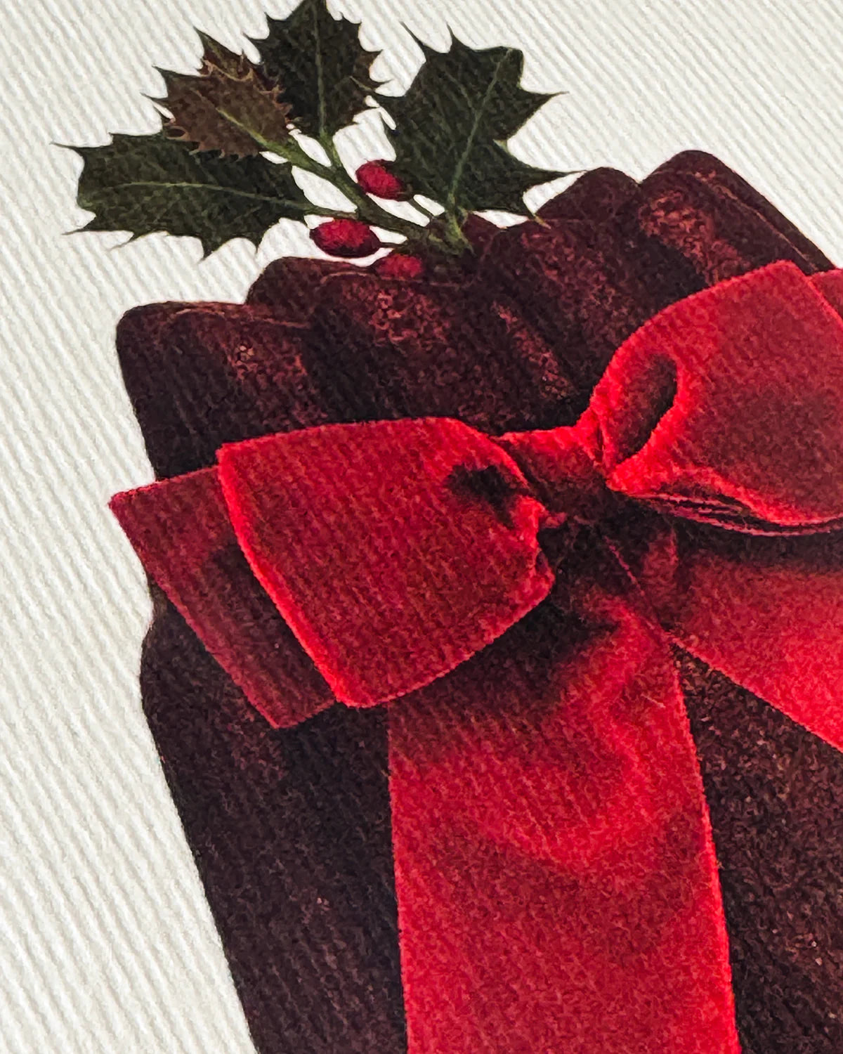 Red velvet bow on a plum pudding with holly leaves and berries.