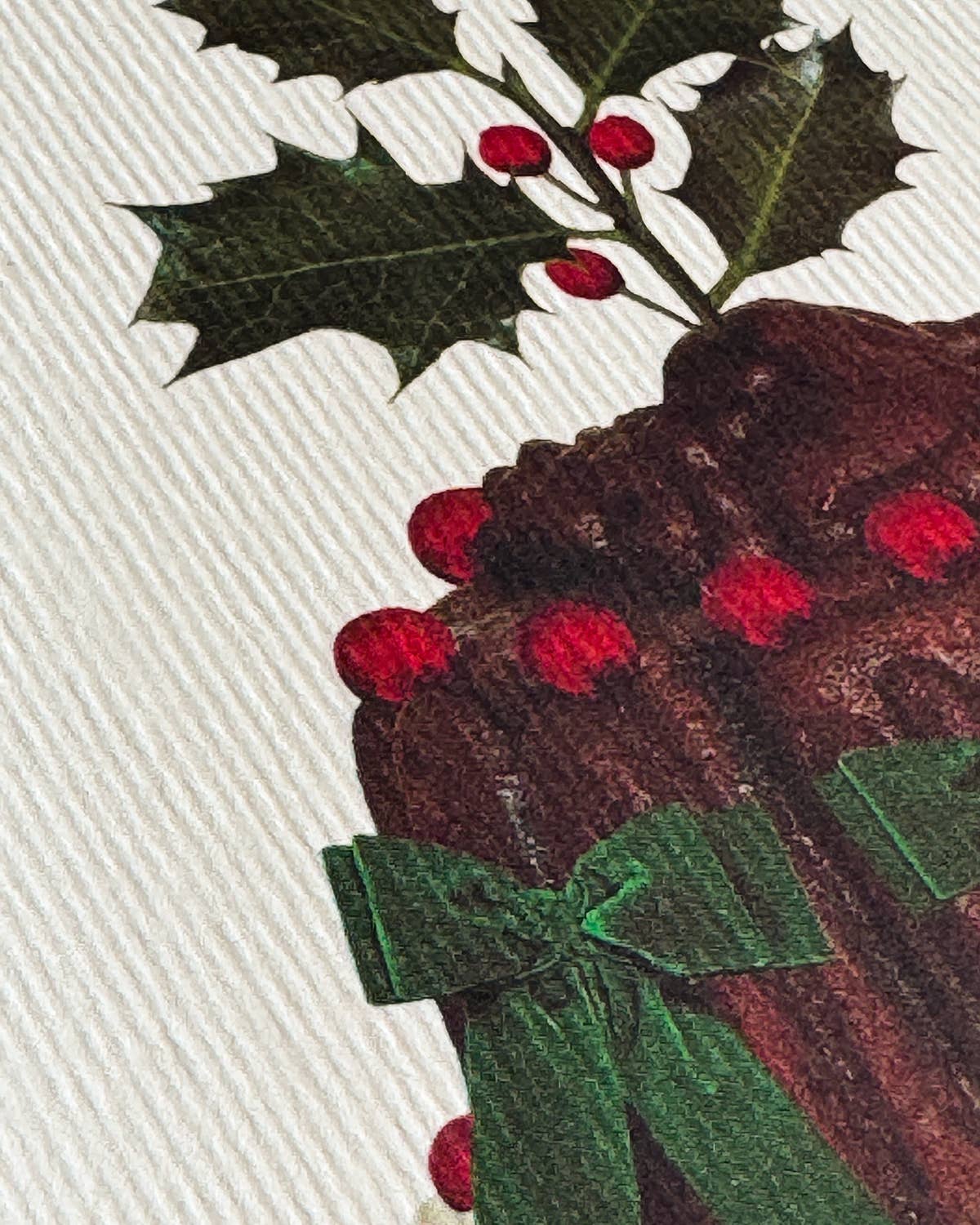 Close up of Christmas pudding with holly leaves and berries on a white fabric background.