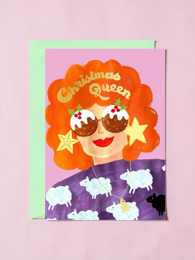 Greeting card with a festive design of a woman with red hair, sunglasses, and Christmas pudding sunglasses on a pink background.