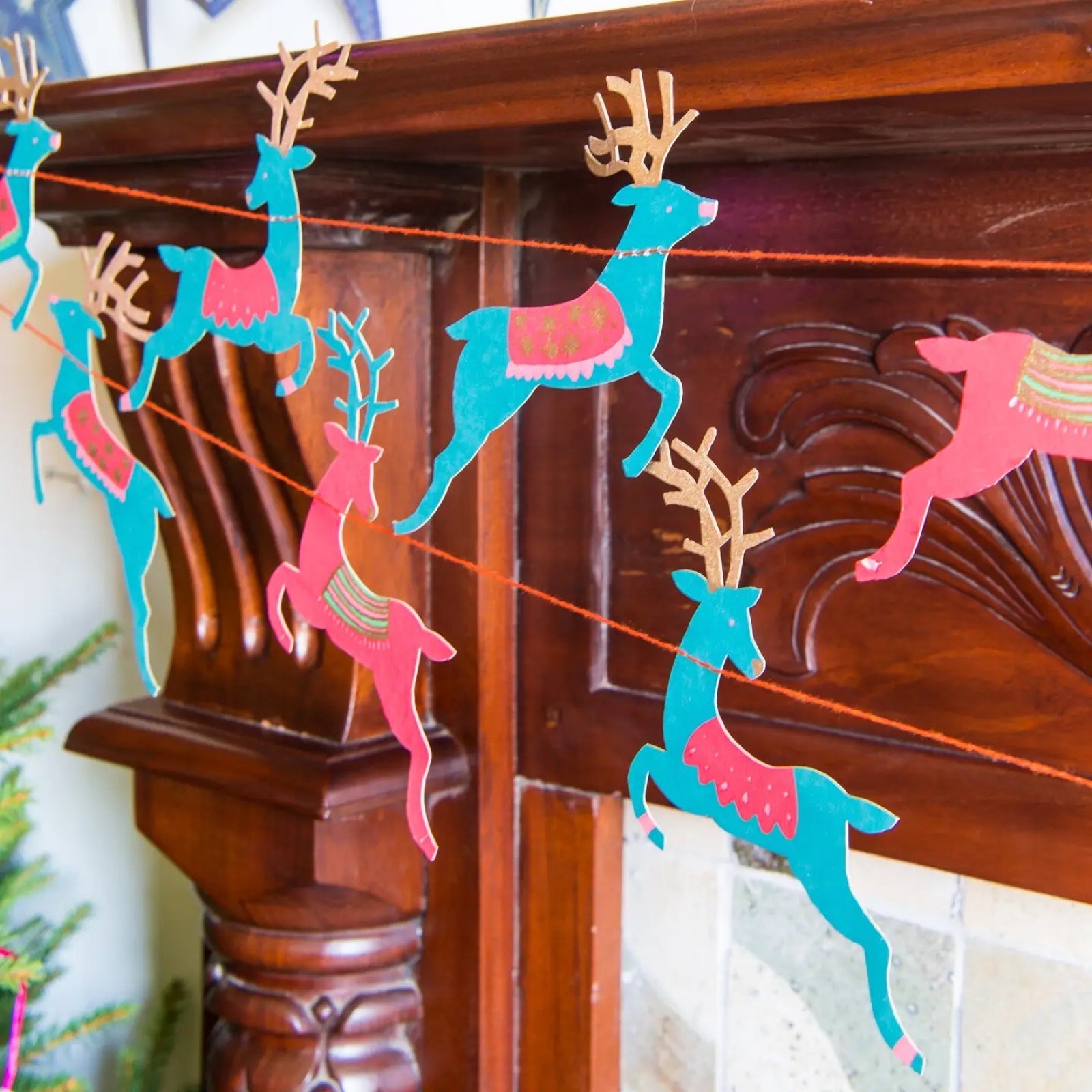 A paper garland with 14 reindeer shapes in red and green hanging on a wooden mantlepiece.