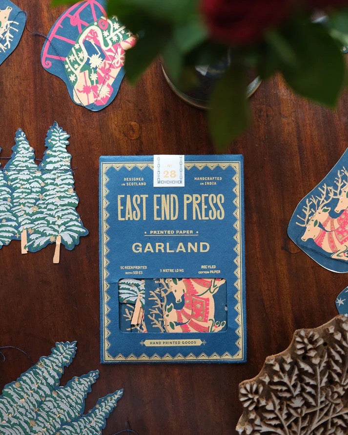 A skyline paper garland featuring Christmas trees, sleighs and reindeer on s table, with packaging.