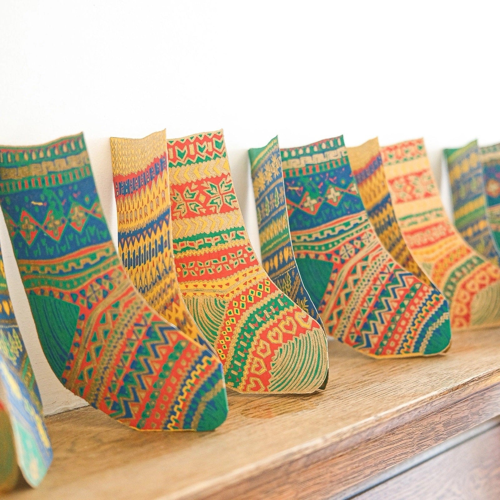 Christmas stockings concertina garland measures three metres long and is hand-printed on recycled paper in shades of green, yellow and red on a wooden shelf.