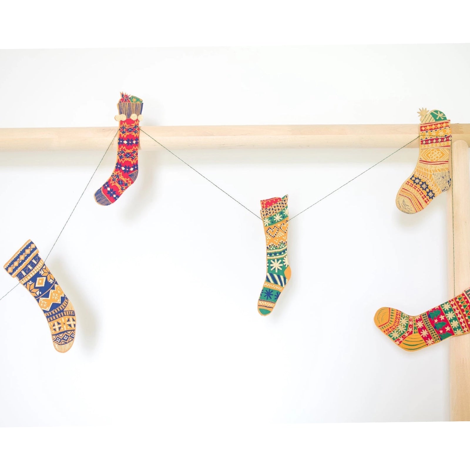 Festive stockings garland, featuring ten screen-printed Christmas Stockings in gold, green, red and blue patterns hanging on a wooden bed frame.