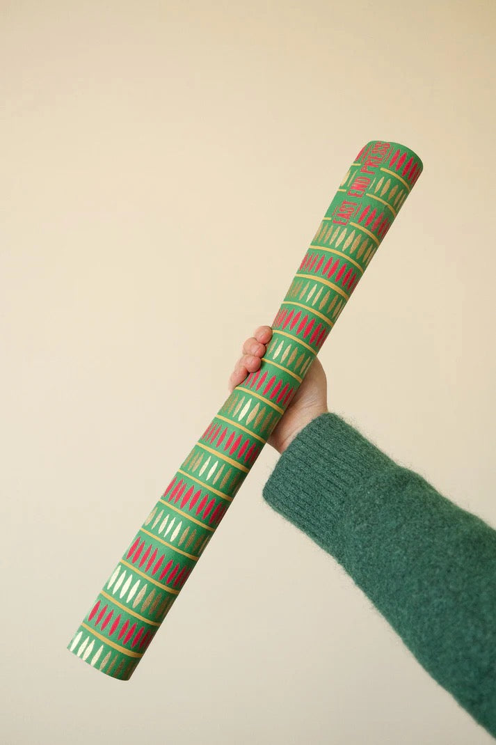 Hand holding a roll of green and red patterned paper against a beige background.