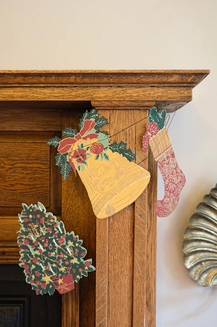 Decorative Christmas elements on a wooden mantel including a bell, holly leaves, and stockings.