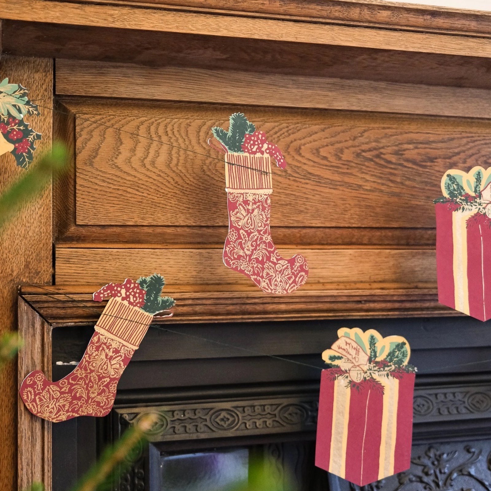 Traditional Christmas paper garland, featuring screen-printed Christmas trees, bells, stockings and presents hanging from a wooden fireplace.