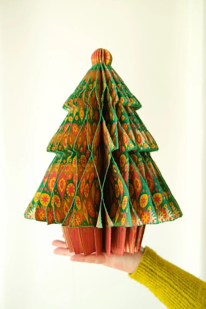 Hand holding a colourful folded paper tree against a white background.