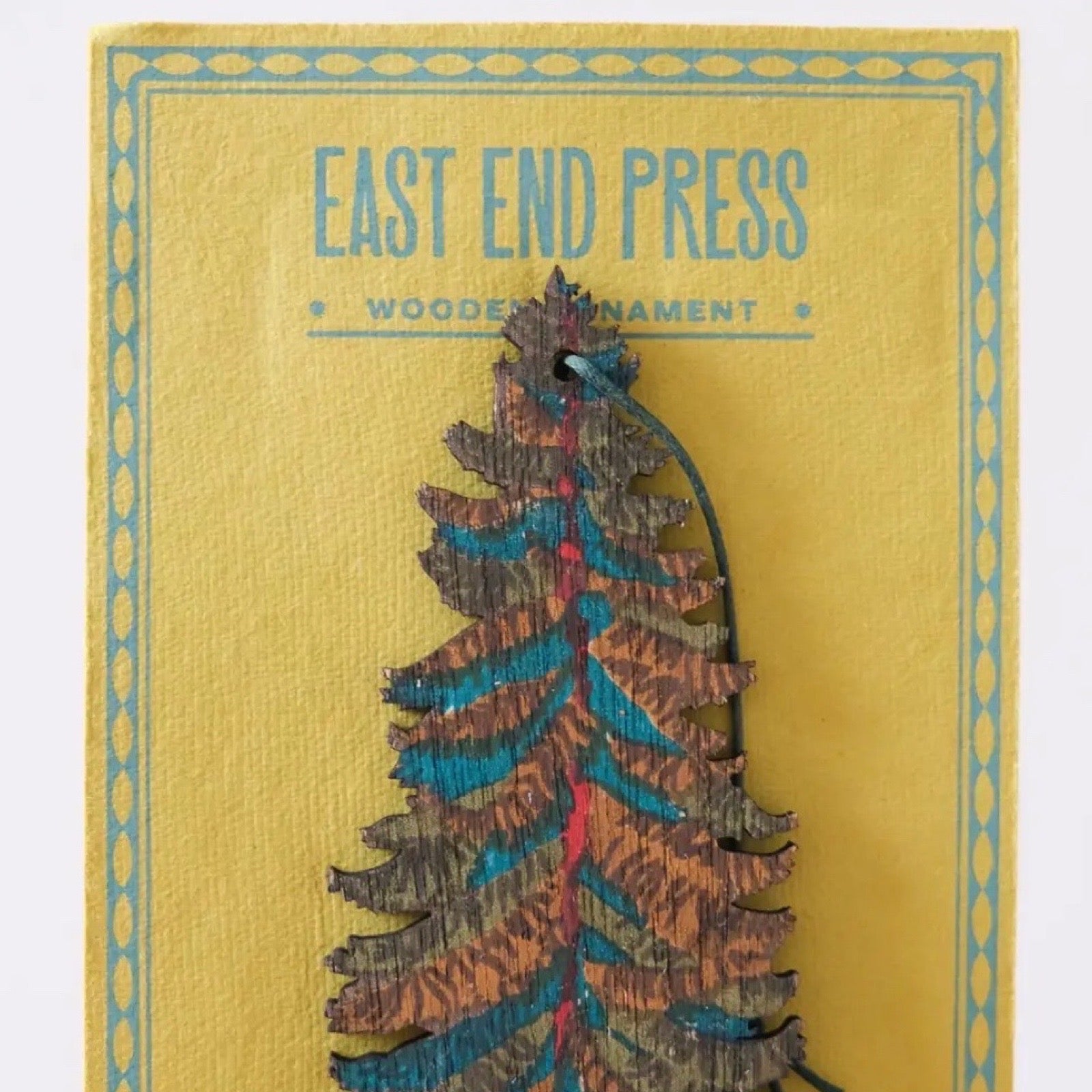 Wooden ornament with 'East End Press' branding on a yellow background.