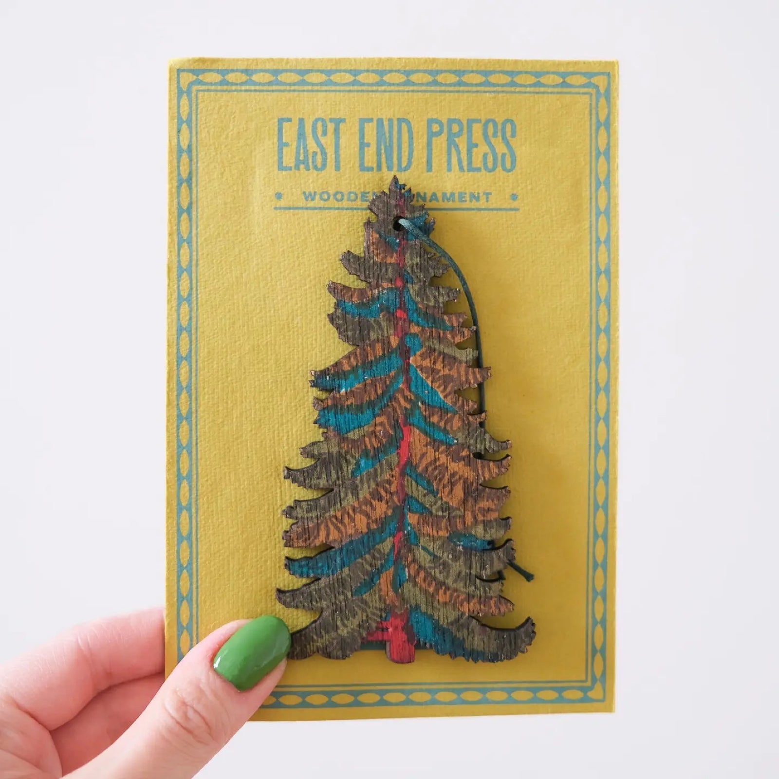 A wooden Christmas tree shaped hanging decoration on a yellow backing card.