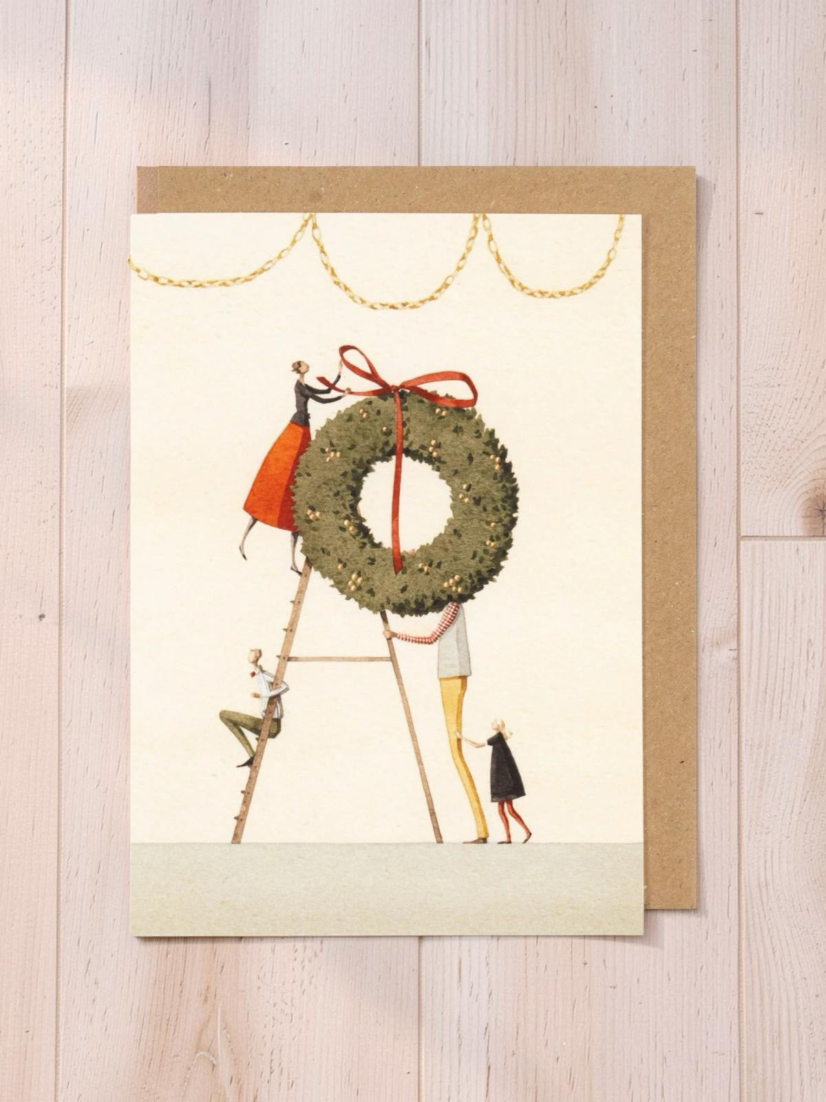 Greeting card with illustration of a wreath and people on a wooden surface.