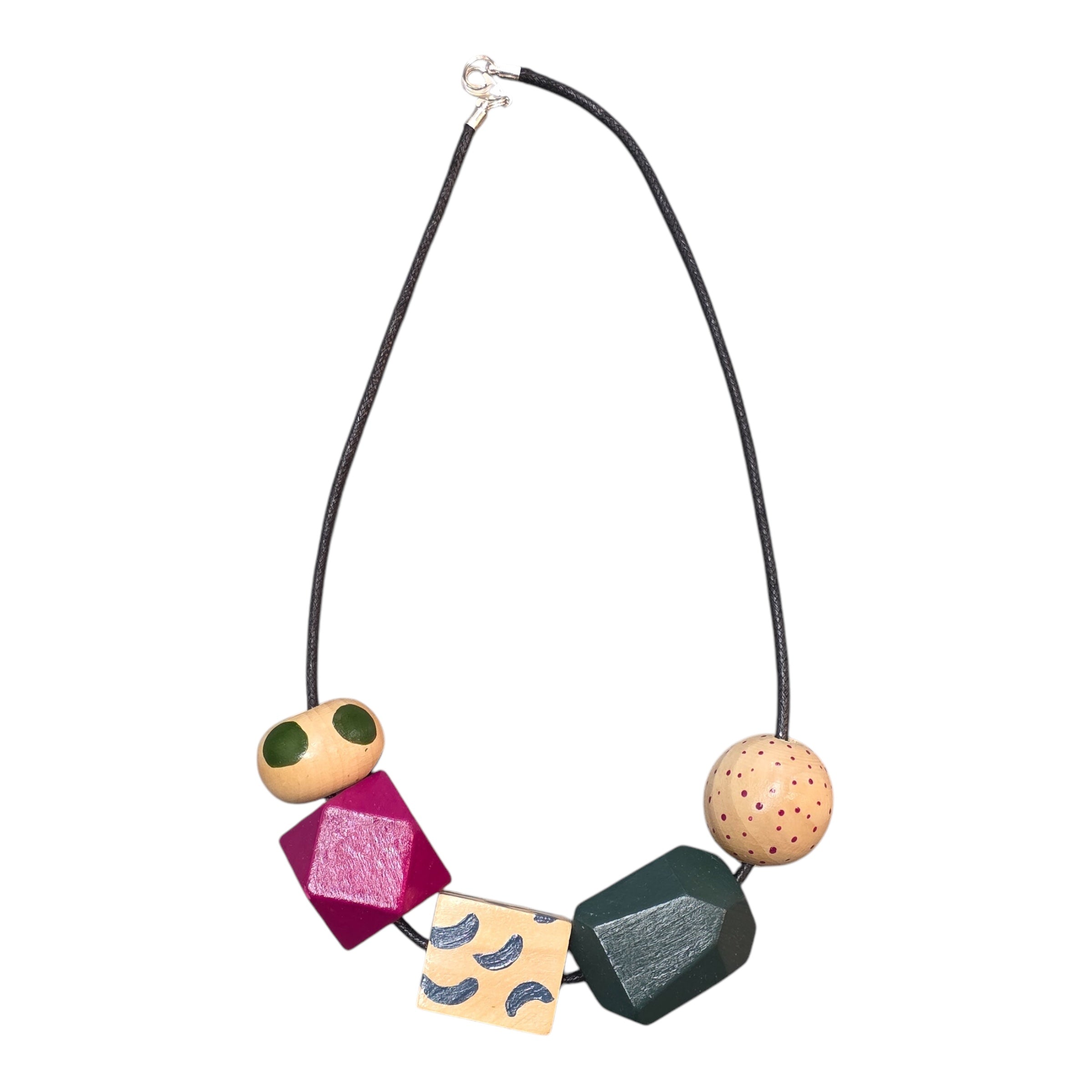 A chunky wooden necklace with 5 large colourful hand-painted beads, 1 white sphere with pink dots, 1 blue, 1 rectangle with green dashes, 1 pink and 1 circular with green polka dots on a black cord with silver coloured clasp.