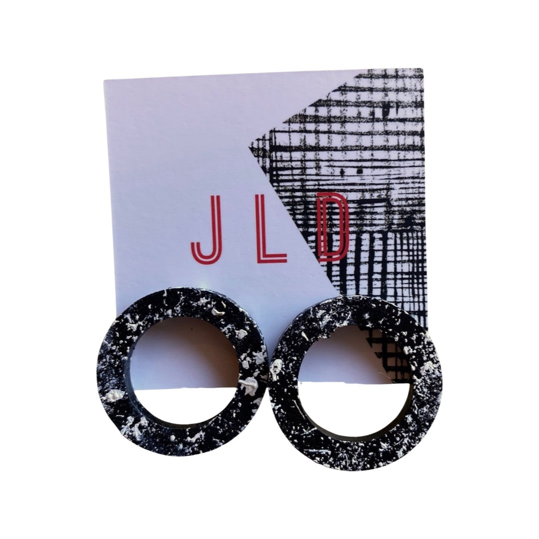 A pair of round hoop earrings with a black and white splash design, silver plated studs, on backing card.