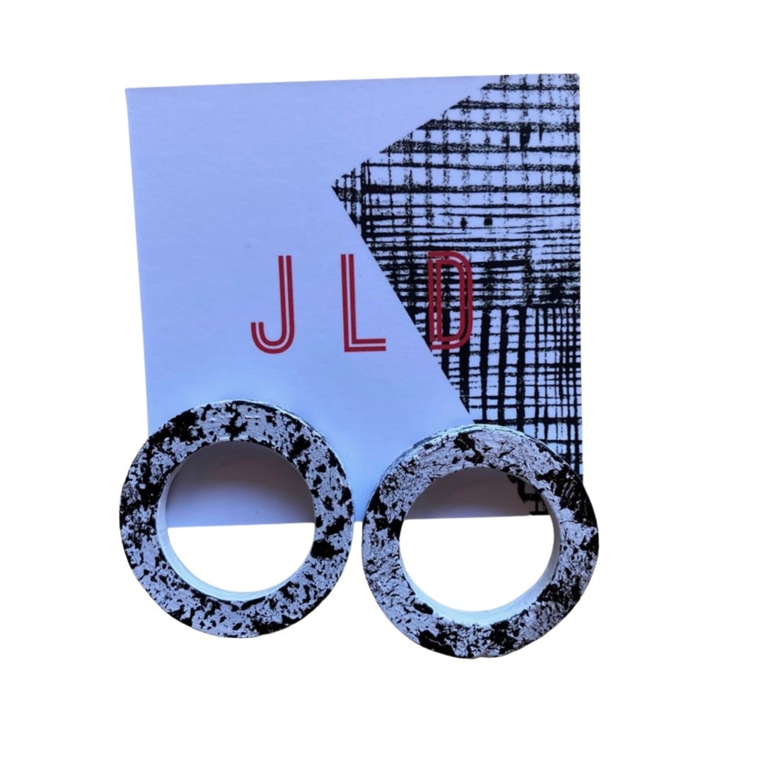 A pair of round hoop earrings with a black and white splash design, silver plated studs, on backing card.