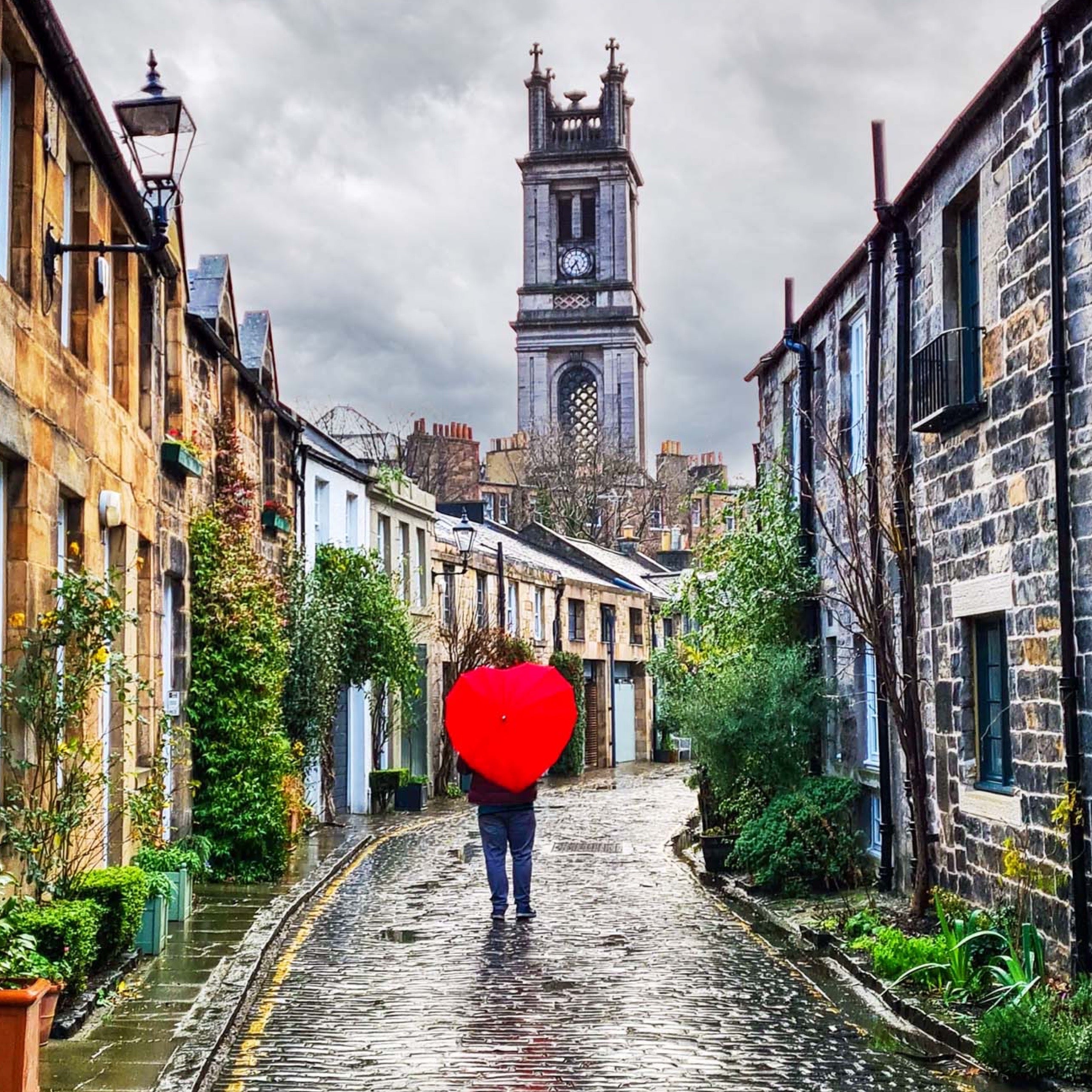 An image of Circus Lane and a person walking with a love heart shaped umbrella. 