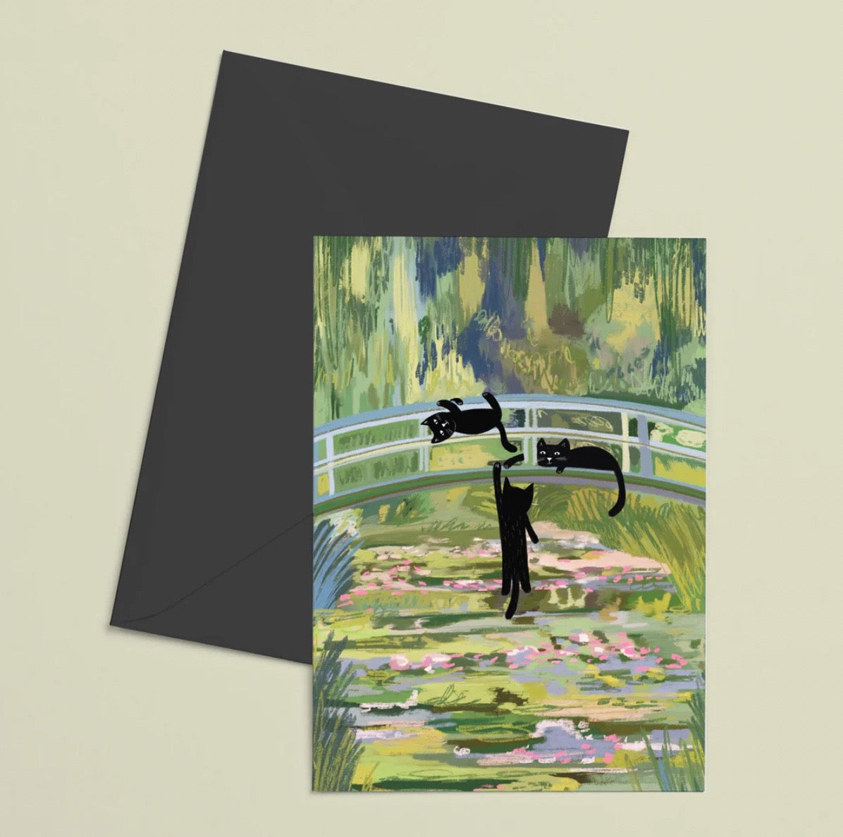 Greeting card with black cats on a bridge over water lilies and a matching black envelope.