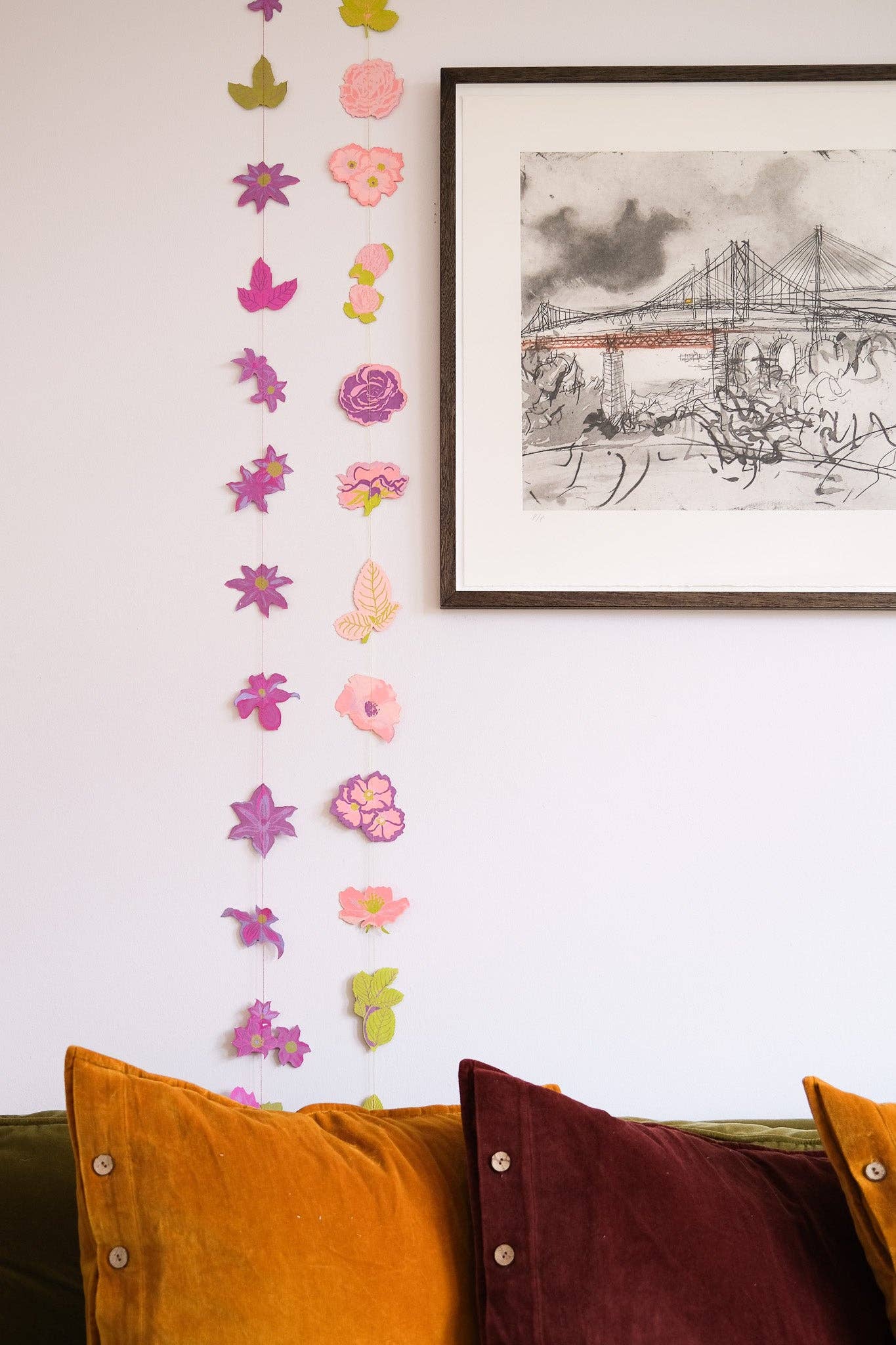 Decorative wall with colourful paper flowers in a living room with a sofa and wall art.