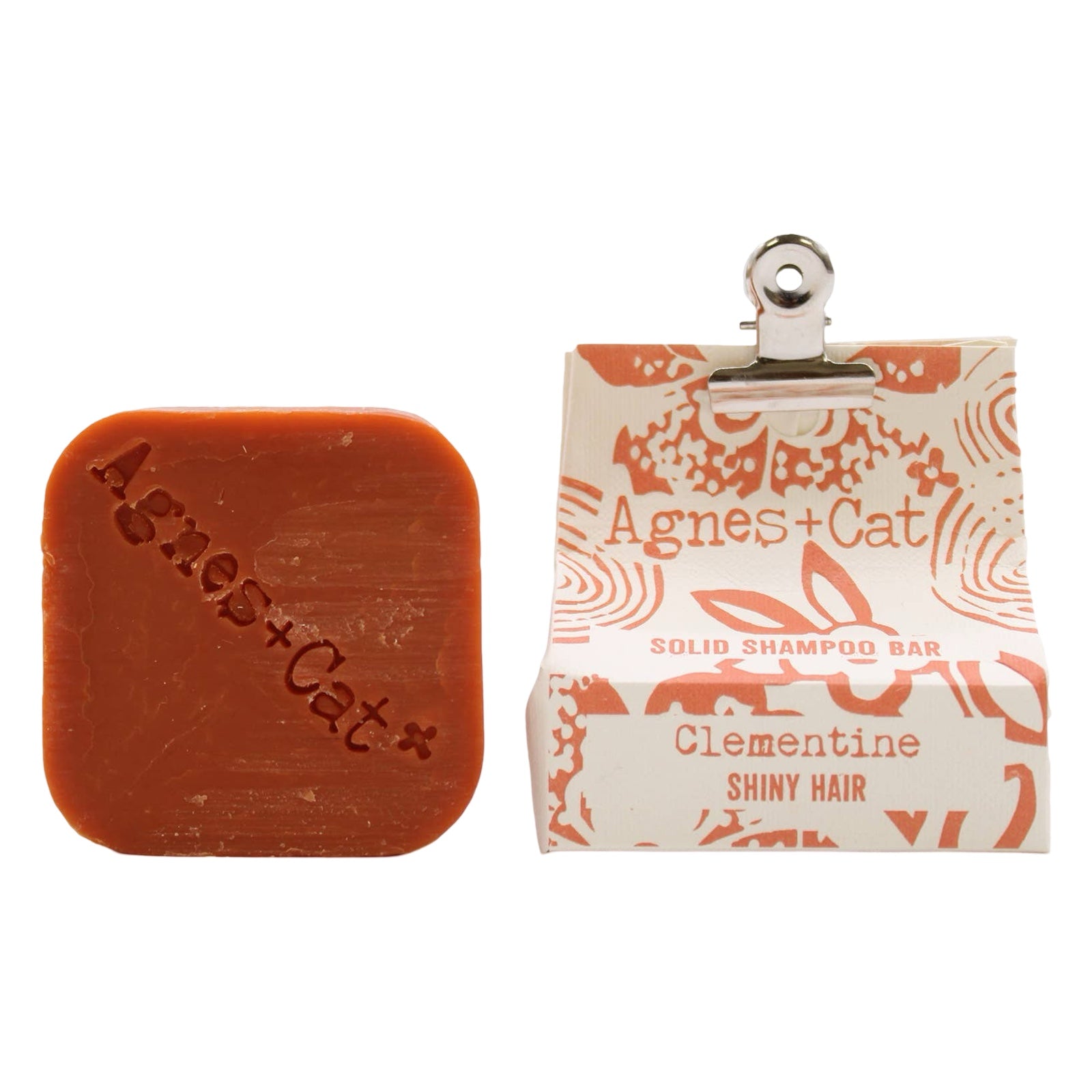 A square-shaped orange, clementine scented dry shampoo bar and a white and orange packet held closed with a bulldog clip.