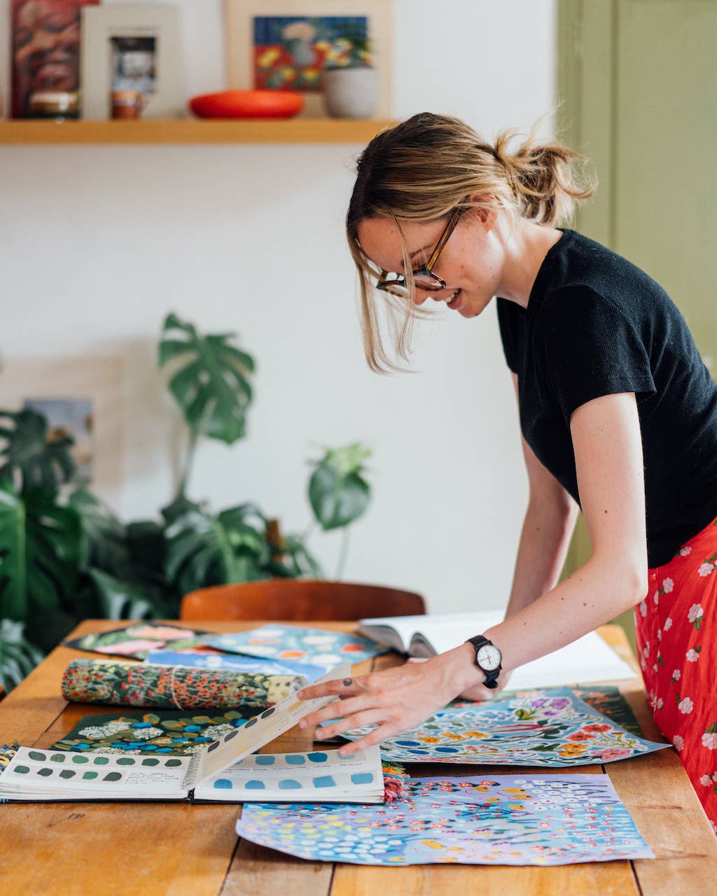 Woman in a home setting looking at art prints on a table.