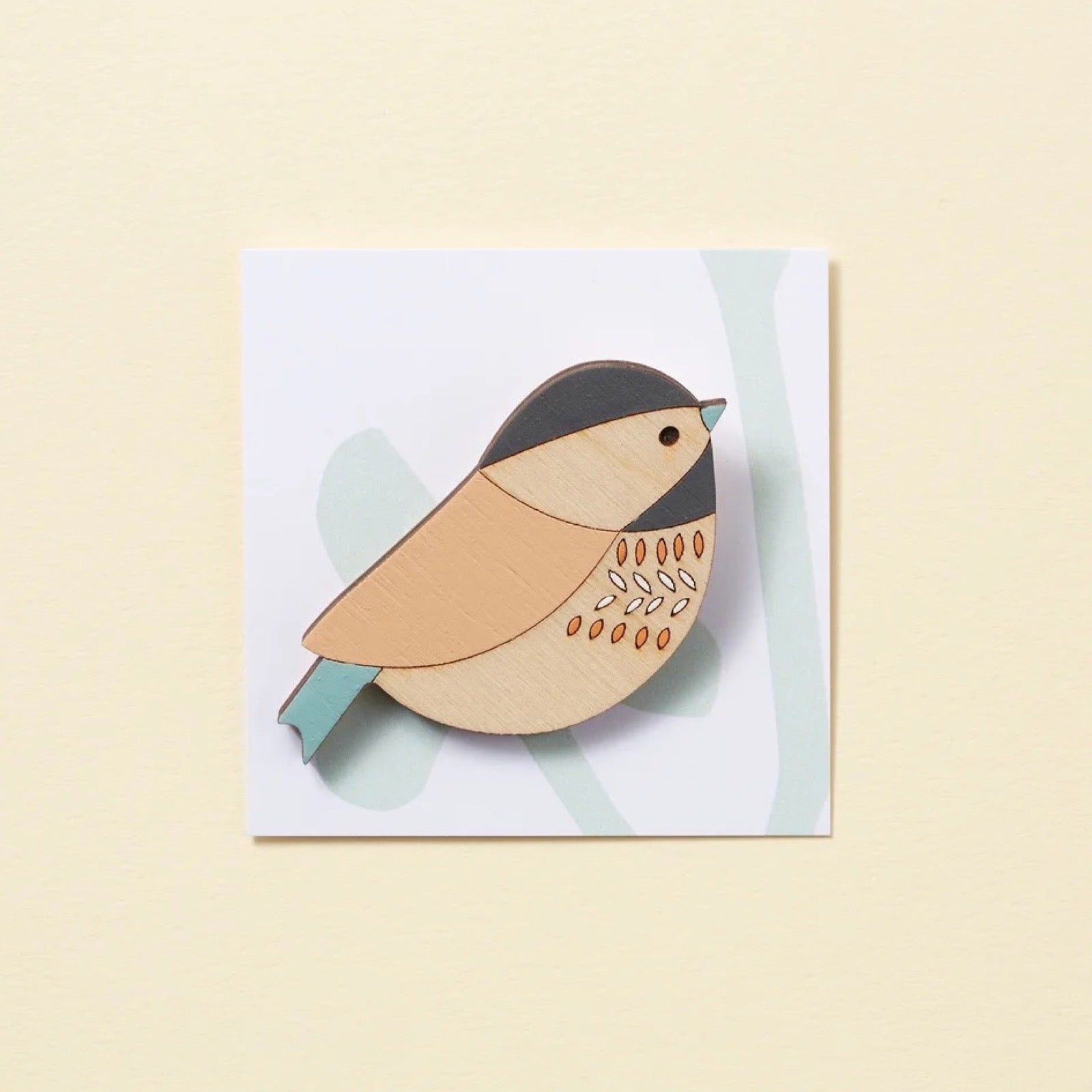 Wooden bird brooch on a white card with a light yellow background.