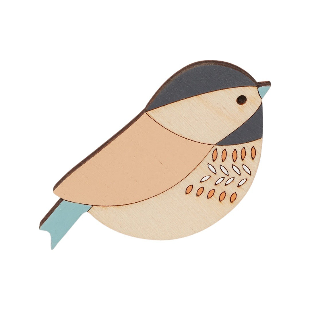 A coaltit-shaped wooden brooch with a navy head, pale orange wing and turquoise tail.