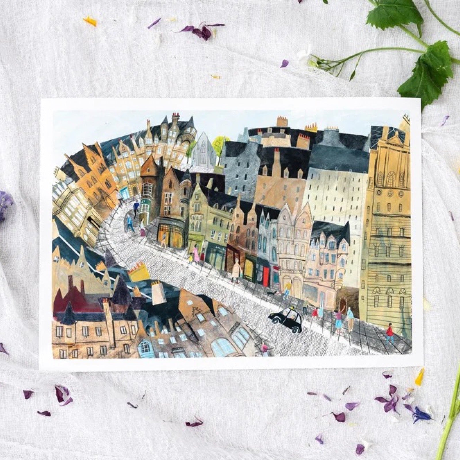 Art print of a street in Edinburgh, sat on fabric, surrounded by petals and leaves.