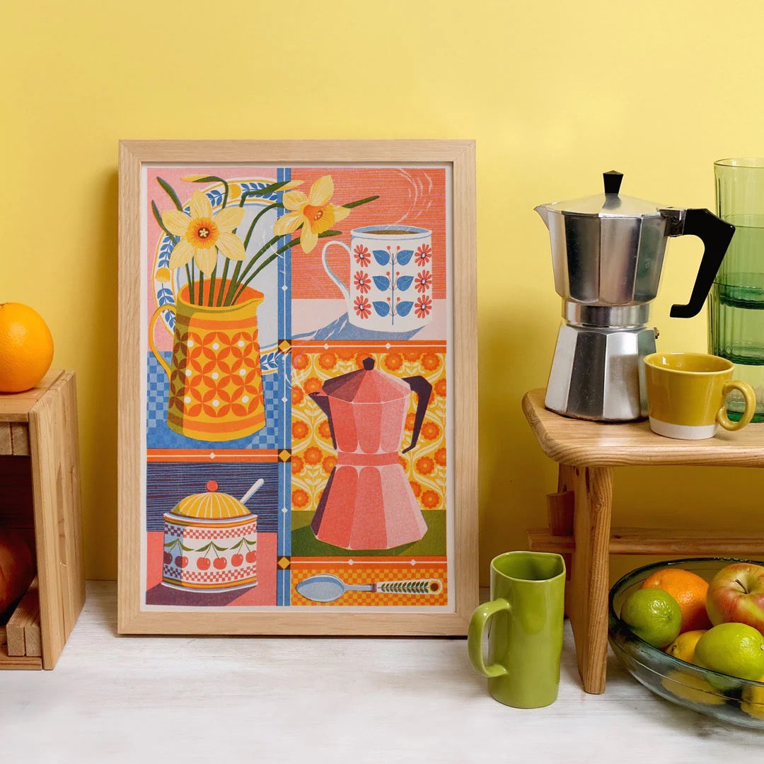 Colorful kitchen-themed artwork in a wooden frame on a yellow wall with kitchen items around.
