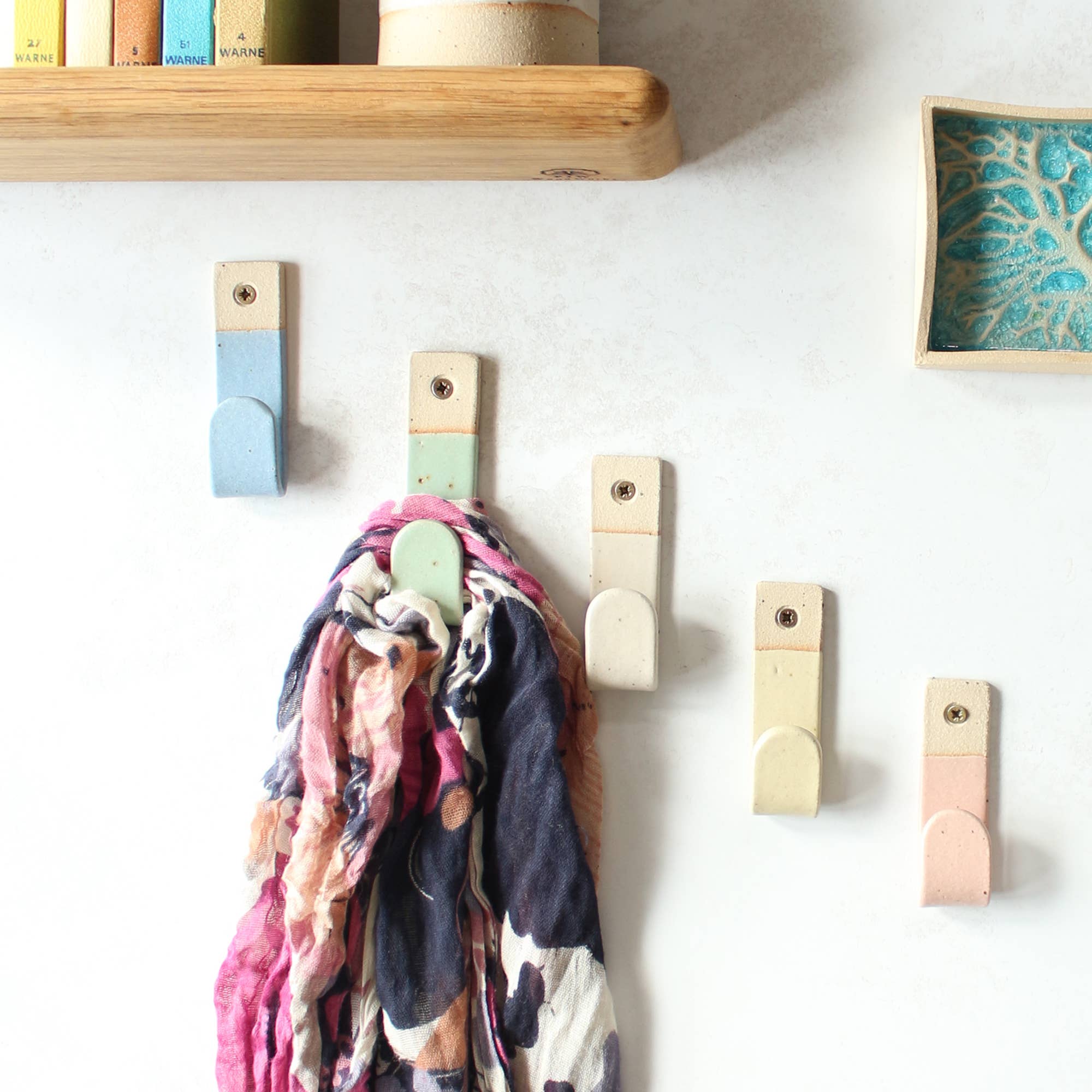  5 pastel coloured stoneware hooks hanging o a wall