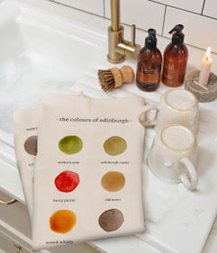 Tea towel with color swatches on a kitchen counter with cleaning products and a mug.