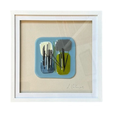 A square fused glass wall hanging, set in a white frame. This glass square is a soft blue, with green, grey, and cream squares and black and white stripe details.