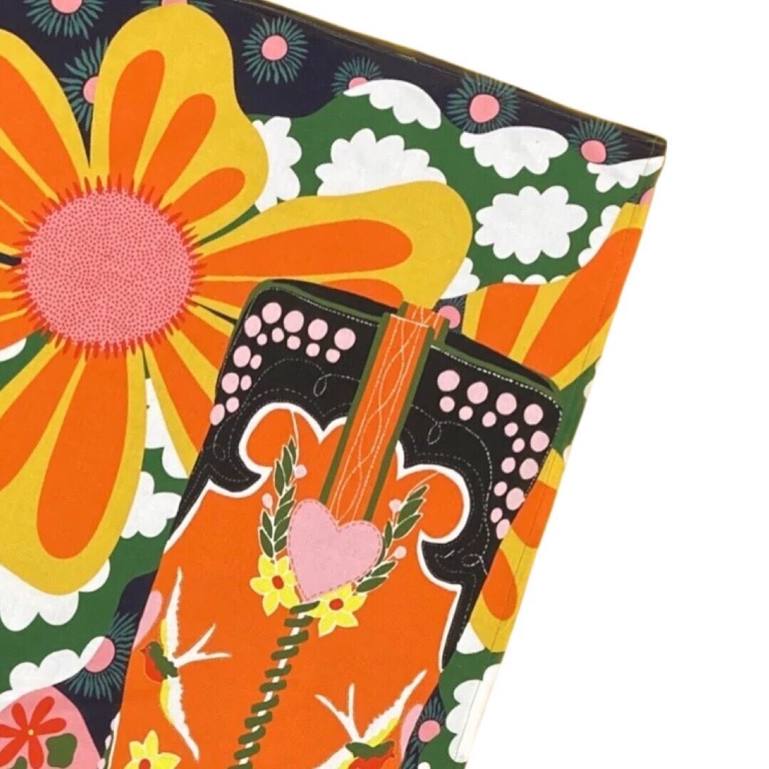 Tea towel featuring a red, black and green cowboy boot surrounded by large yellow and orange flowers and colourful patterns.
