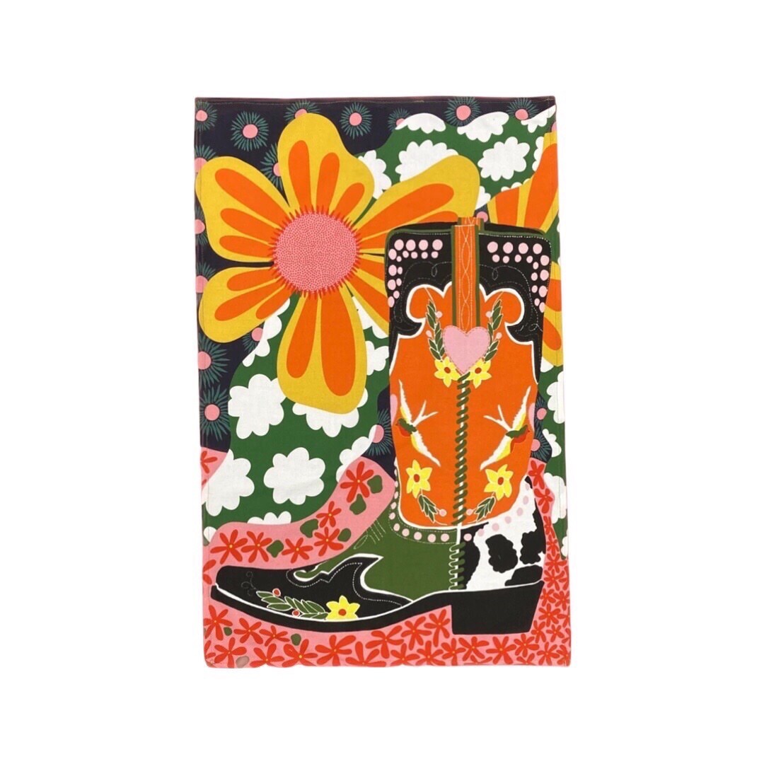 Tea towel featuring a red, black and green cowboy boot surrounded by large yellow and orange flowers and colourful patterns.