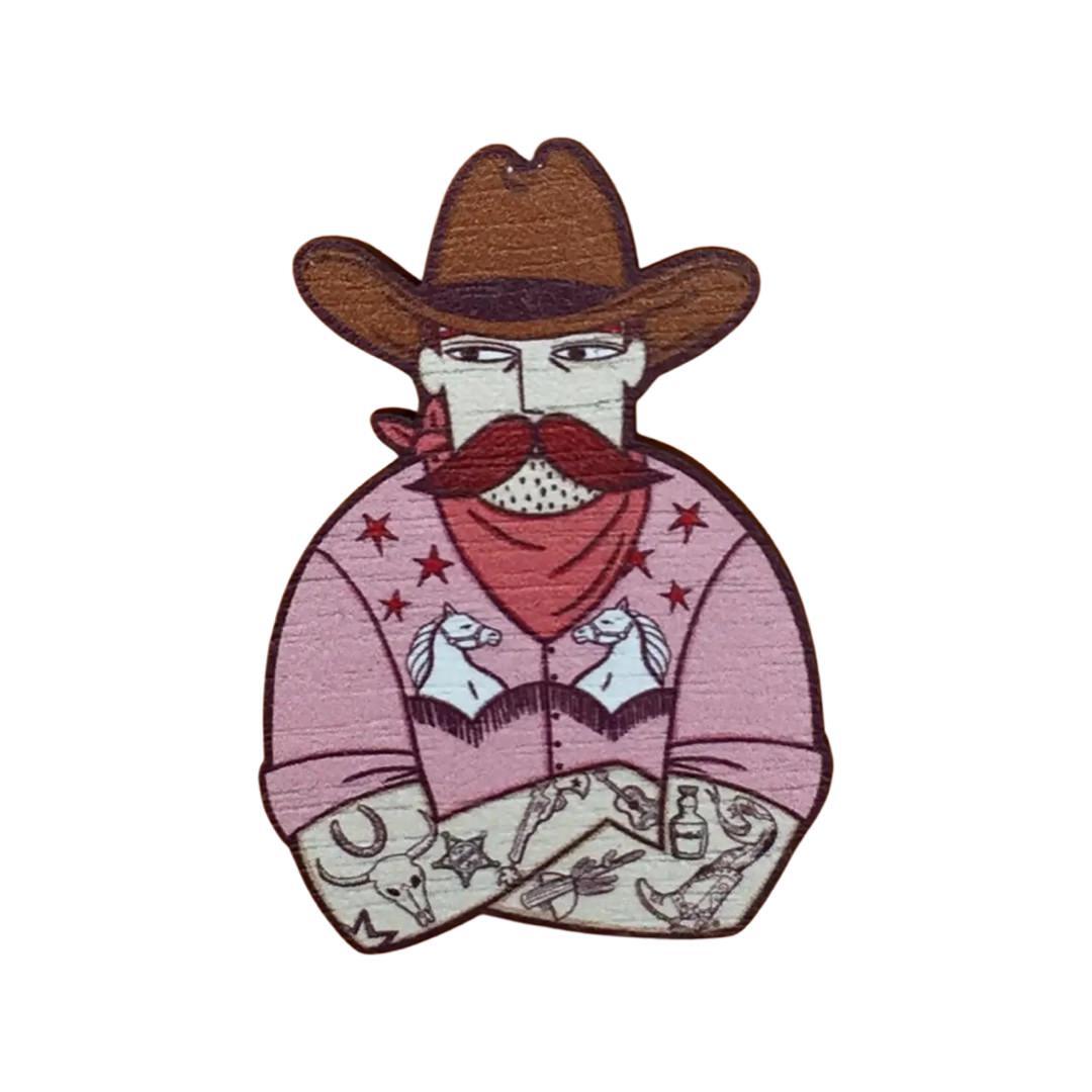 Wooden cowboy brooch featuring a tattooed cowboy wearing a pink shirt with a white horse design, a red neckerchief and a brown cowboy hat.